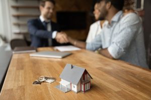 Model house and keys on a desk while a couple shakes hands with a professional